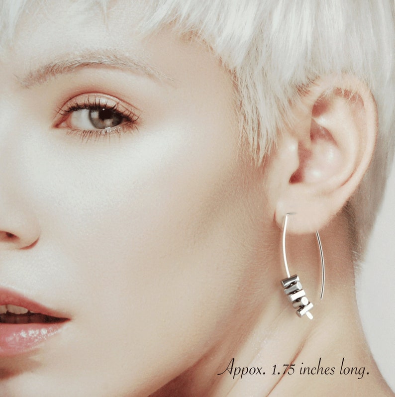 May include: Silver-toned earrings with a curved design, featuring a cluster of small, dark gray geometric beads. The earrings are approximately 1.75 inches long.