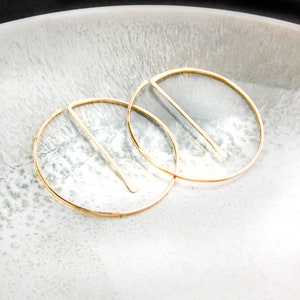 Peut inclure: Une paire de boucles d'oreilles cr&eacute;oles en or avec un design en ligne droite. Les boucles d'oreilles sont sur une surface blanche.