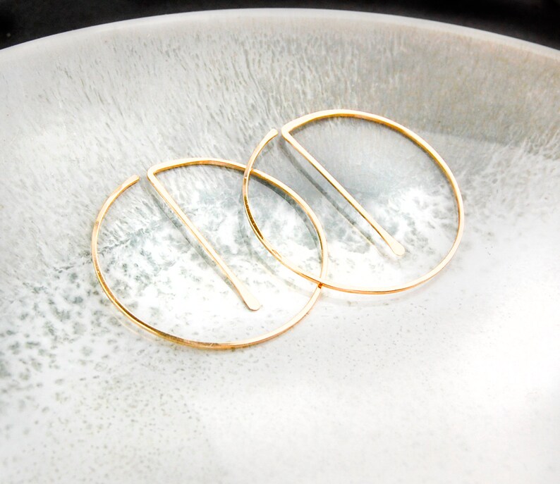 Peut inclure: Une paire de boucles d'oreilles cr&eacute;oles en or avec un design en ligne droite. Les boucles d'oreilles sont sur une surface blanche.