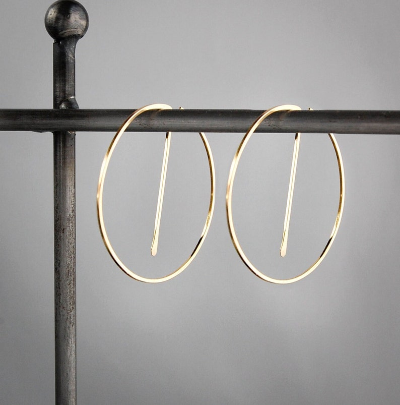 Peut inclure: Une paire de boucles d'oreilles cr&eacute;oles en or avec un design en ligne droite. Les boucles d'oreilles sont suspendues &agrave; un support en m&eacute;tal noir.