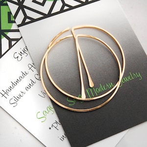 Peut inclure: Une paire de boucles d'oreilles cr&eacute;oles en or avec une finition martel&eacute;e. Les boucles d'oreilles sont compos&eacute;es de deux cercles, l'un l&eacute;g&egrave;rement plus grand que l'autre. Les boucles d'oreilles sont sur une carte blanche avec le texte "Sage Modern Jewelry".