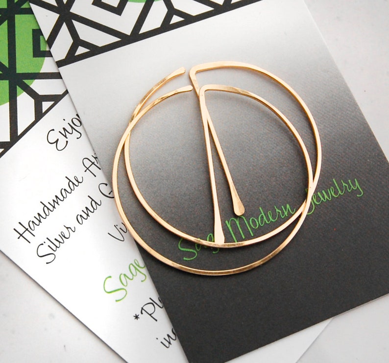 Peut inclure: Une paire de boucles d'oreilles cr&eacute;oles en or avec une finition martel&eacute;e. Les boucles d'oreilles sont compos&eacute;es de deux cercles, l'un l&eacute;g&egrave;rement plus grand que l'autre. Les boucles d'oreilles sont sur une carte blanche avec le texte "Sage Modern Jewelry".