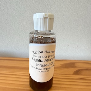 May include: A clear glass bottle with a white cap, containing a dark brown liquid. The label reads "Karibu Harvest Herbs and Spices Kigelia Africana Infused Oil 100% Pure Organic & Natural 60ml/2fl.oz".