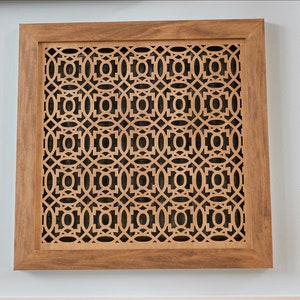 May include: A wooden framed vent cover with a decorative geometric pattern cut out. The vent cover is light brown and has a dark brown frame.