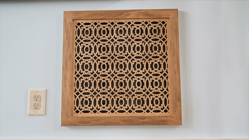 May include: A wooden framed vent cover with a decorative geometric pattern cut out. The vent cover is light brown and has a dark brown frame.