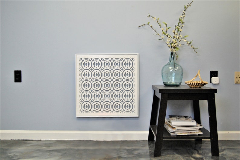 May include: White metal decorative vent cover with a geometric pattern, mounted on a light blue wall. A small black side table with a shelf holds a blue glass vase with white flowers and a woven basket.