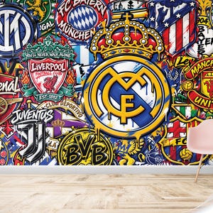 May include: A wall mural featuring a collage of various professional football team logos, including Real Madrid, Manchester United, Liverpool, and Juventus, with a graffiti-style aesthetic. The text ANY TEAM IN THE MIDDLE is printed in the bottom right corner.