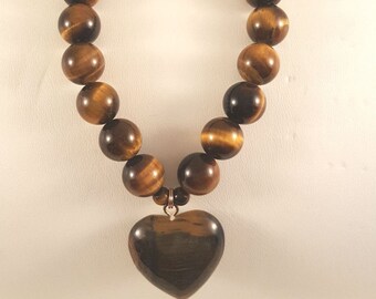 May include: A bracelet featuring large, round, tiger's eye beads in shades of brown and gold. A heart-shaped tiger's eye pendant hangs from the center. The bracelet is strung on a stretchy cord.