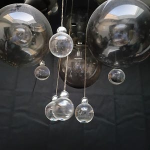 May include: A multi-light pendant fixture featuring a circular chrome ceiling mount with several suspended glass spheres. The design includes large, dark-tinted glass globes interspersed with smaller, clear glass orbs hanging from thin metal chains.