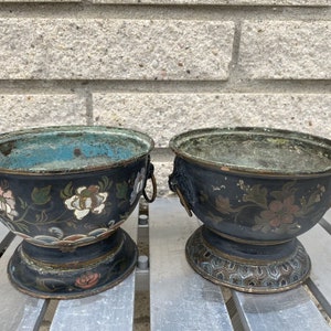 May include: Two antique black metal bowls with floral designs and gold accents. The bowls have a green patina and are on a wooden surface.