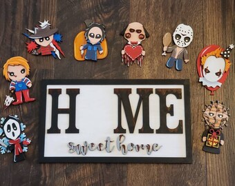 May include: A white sign with the words "HOME" in black letters and "sweet home" in silver letters.  The sign is surrounded by eight horror movie character figurines, including Freddy Krueger, Jason Voorhees, and Michael Myers.