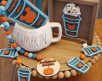 May include: A wooden sign with a blue and orange pumpkin spice latte design. The sign says "Pumpkin Spice Junkie". The sign is sitting on a wooden tray with a white mug that says "Pumpkin" and a garland of blue and orange beads with pumpkin spice latte charms.