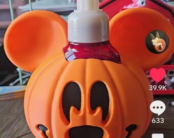 May include: An orange Mickey Mouse-shaped soap dispenser with a pumpkin design. The dispenser has black eye and mouth cutouts, and large orange ears. The pump is white, and the liquid inside is red. A fun, festive item for Halloween.