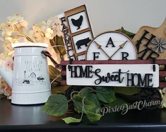 May include: A white wooden wagon filled with farmhouse decor, including a sign that reads "HOME Sweet HOME", a round sign with the letters "FAR", a wooden cutting board with the word "HOME" and a windmill design, and a white watering can with the text "Raise a Country Sunshine".