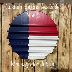 May include: A round wooden shelf painted in the colors of the North Carolina flag. The shelf has multiple tiers and is decorated with a gold star and the letters "N*C".