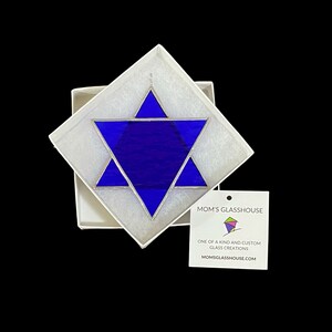 May include: A blue stained glass Star of David in a white box with a tag that reads "Mom's Glasshouse, One of a kind and custom glass creations, Momsglasshouse.com"