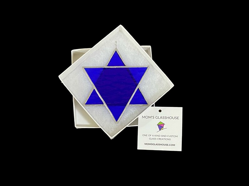 May include: A blue stained glass Star of David in a white box with a tag that reads "Mom's Glasshouse, One of a kind and custom glass creations, Momsglasshouse.com"