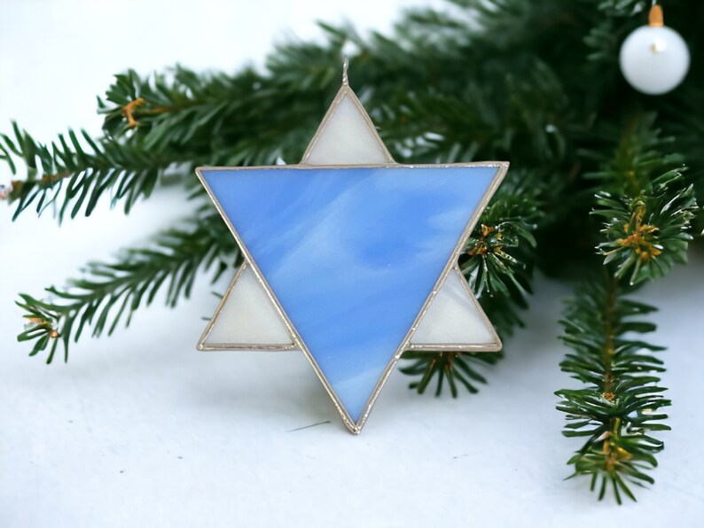 May include: A blue and white stained glass Star of David ornament. The star is made of glass and has a silver frame.