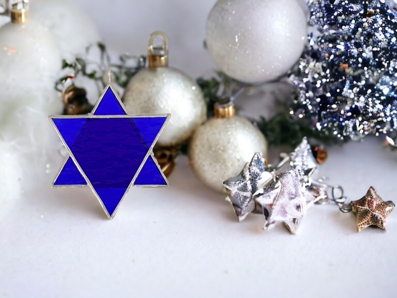 May include: A blue glass Star of David ornament with silver trim, surrounded by white and silver Christmas ornaments.