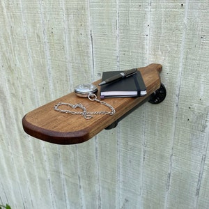 K&ouml;nnte beinhalten: Ein Holzregal mit schwarzen Metallrohrst&uuml;tzen. Das Regal ist an einer wei&szlig;en Holzwand montiert. Eine Taschenuhr, ein Stift und ein Notizbuch liegen auf dem Regal.