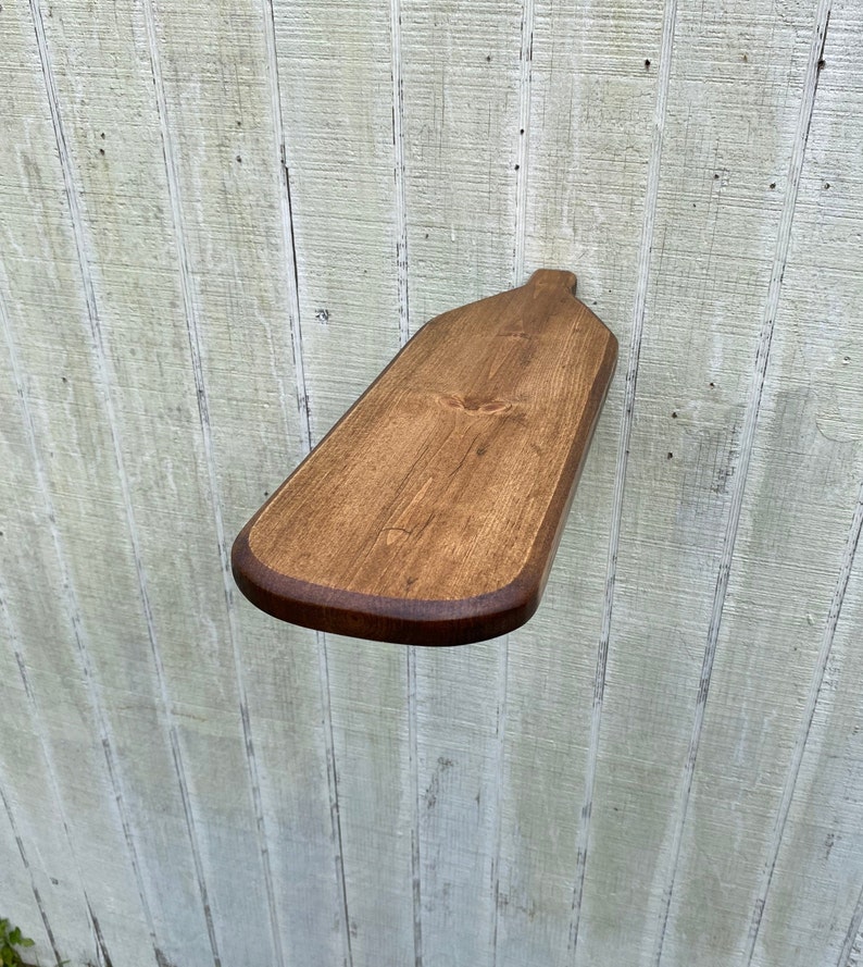 K&ouml;nnte beinhalten: Ein Holzbrett zum Servieren in Form einer Flasche, in einem dunklen Braunton gebeizt. Das Brett hat eine abgerundete Kante und eine glatte Oberfl&auml;che.