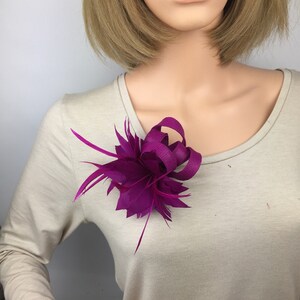 May include: A magenta feather and ribbon flower brooch. The flower is made of feathers and a ribbon that is tied in a bow. The brooch is a great addition to any outfit.