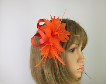 May include: Orange feather flower hair clip. The flower is made of feathers and has a red ribbon accent.