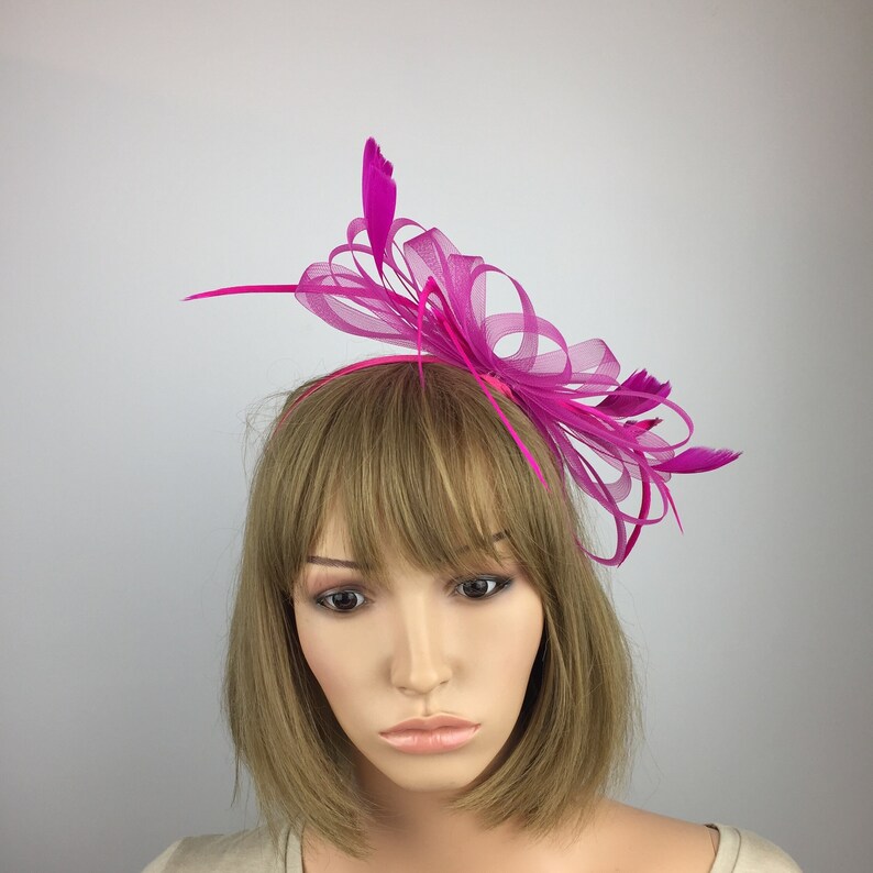 May include: A fuchsia pink feather and tulle headband with a large bow. The headband is worn on a mannequin with short brown hair.