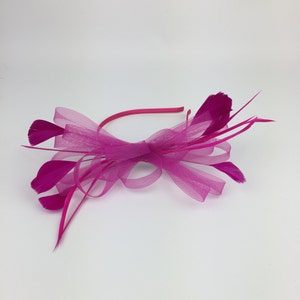 May include: A pink headband with a large bow and feathers. The headband is made of a soft, stretchy material and is perfect for adding a touch of elegance to any outfit.