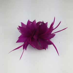 May include: A magenta feather flower hair clip. The flower is made of multiple layers of feathers and has a small ribbon in the centre.