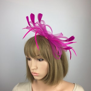 May include: A pink feather and tulle headband with a large bow. The headband is worn on a mannequin with short brown hair.