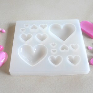 Puede incluir: Un molde de silicona blanco con 12 cavidades en forma de coraz&oacute;n. El molde est&aacute; lleno de caramelos en forma de coraz&oacute;n rosa.