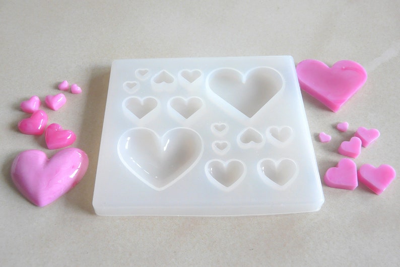 Puede incluir: Un molde de silicona blanco con 12 cavidades en forma de coraz&oacute;n. El molde est&aacute; lleno de caramelos en forma de coraz&oacute;n rosa.