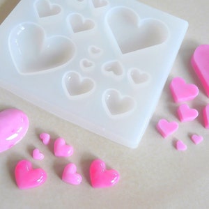 Puede incluir: Un molde de silicona con m&uacute;ltiples cavidades en forma de coraz&oacute;n, junto con varios caramelos en forma de coraz&oacute;n rosa hechos con el molde.