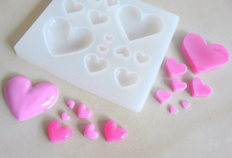 Puede incluir: Un molde de silicona con m&uacute;ltiples cavidades en forma de coraz&oacute;n, junto con varios caramelos en forma de coraz&oacute;n rosa hechos con el molde.