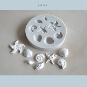 Könnte beinhalten: Eine Silikonform mit 8 verschiedenen Formen von Muscheln und Seesternen. Die Form ist weiß und wird neben 8 weißen Muscheln und Seesternen gezeigt.