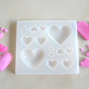 Puede incluir: Un molde de silicona con 12 cavidades en forma de coraz&oacute;n, perfecto para hacer peque&ntilde;os caramelos o jabones en forma de coraz&oacute;n rosa. El molde se muestra con varios caramelos en forma de coraz&oacute;n rosa.