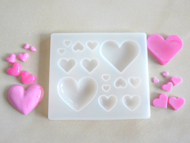 Puede incluir: Un molde de silicona con 12 cavidades en forma de coraz&oacute;n, perfecto para hacer peque&ntilde;os caramelos o jabones en forma de coraz&oacute;n rosa. El molde se muestra con varios caramelos en forma de coraz&oacute;n rosa.