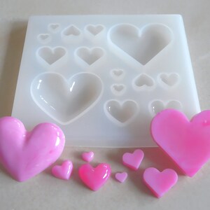 Puede incluir: Un molde de silicona blanco con 10 cavidades en forma de coraz&oacute;n. El molde est&aacute; lleno de corazones de resina rosa de varios tama&ntilde;os.