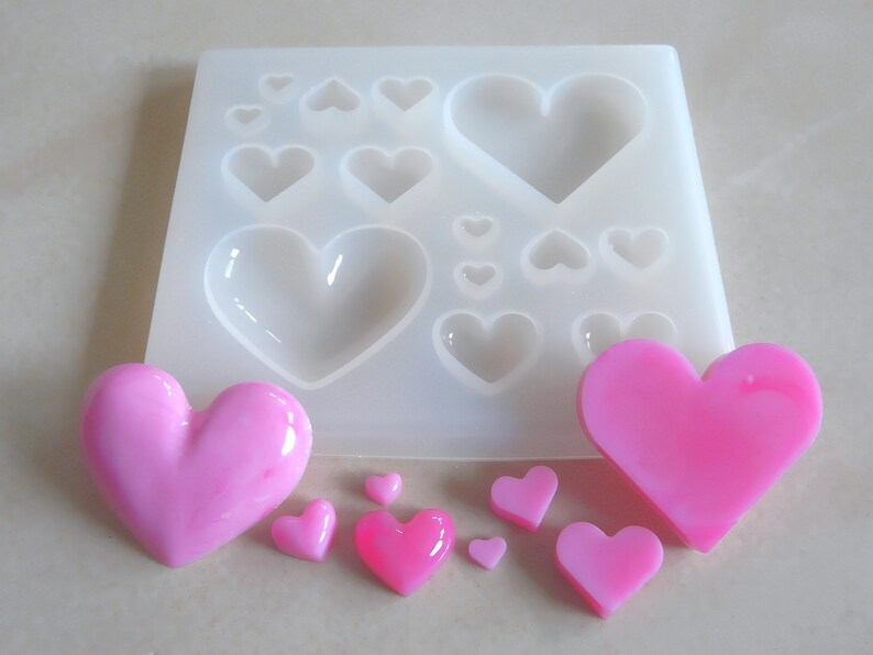 Puede incluir: Un molde de silicona blanco con 10 cavidades en forma de coraz&oacute;n. El molde est&aacute; lleno de corazones de resina rosa de varios tama&ntilde;os.