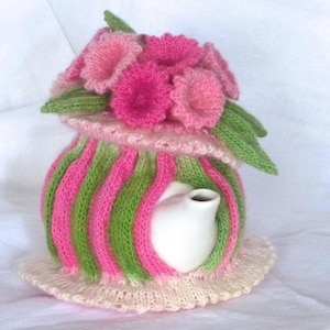Pode incluir: Uma capa de chaleira de tricô rosa e verde com um design floral. A capa é feita de fio macio e tem uma delicada renda.