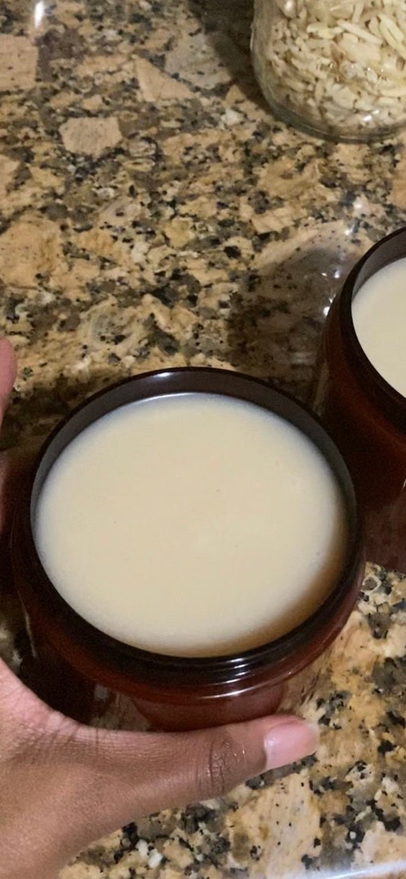 Pu&ograve; includere: Due barattoli marroni pieni di una crema beige chiaro. I barattoli sono su un piano di lavoro macchiato.