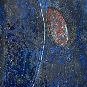Pu&ograve; includere: Primo piano di una piastrella di ceramica blu con una forma ovale di colore rosso ruggine al centro. La piastrella ha una superficie testurizzata e una linea bianca che attraversa in diagonale.