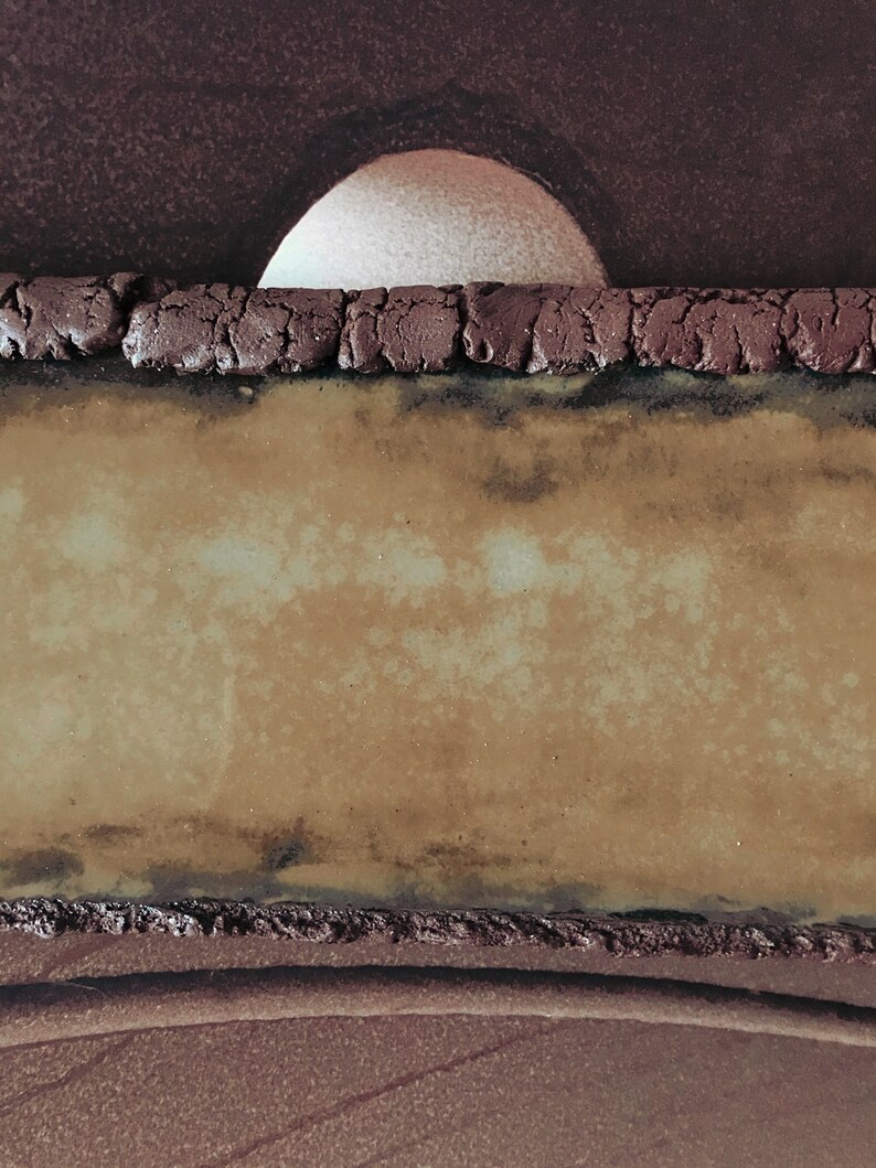 K&ouml;nnte beinhalten: Nahaufnahme einer Keramikplatte mit brauner, strukturierter Oberfl&auml;che. Die Platte hat eine kreisf&ouml;rmige &Ouml;ffnung oben, die einen wei&szlig;en Hintergrund freigibt.