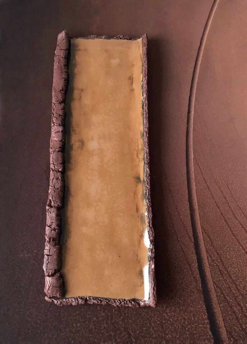 K&ouml;nnte beinhalten: Eine rechteckige Keramikschale mit brauner Glasur und einem erh&ouml;hten Rand. Die Schale hat einen glatten, hellbraunen Innenraum.