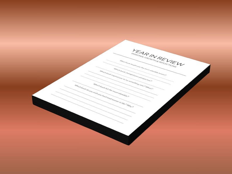 May include: A white Year in Review journal with black edges, featuring prompts for personal growth and reflections. The journal is set against a gradient brown background. The text on the journal includes questions about books and life.