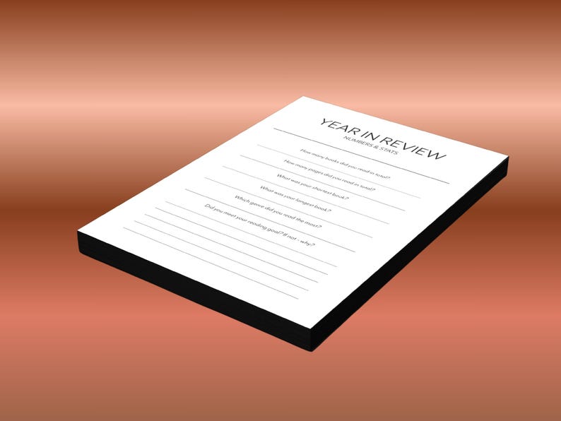 May include: A white Year in Review journal with a black border, lying on a gradient brown background. The journal has lines for recording book-related statistics, such as the number of books read and the longest book.