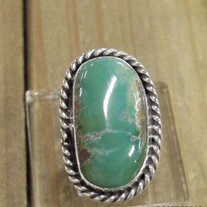 May include: A silver ring with a green turquoise stone set in a rope-like design.