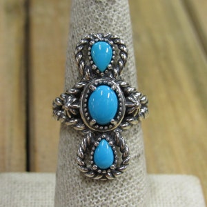 May include: A silver ring with three turquoise stones set in a rope design. The stones are oval and teardrop shaped.