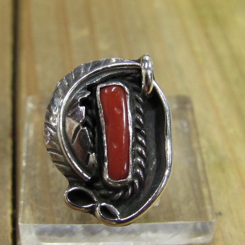 May include: A silver ring with a red coral stone set in a detailed design.
